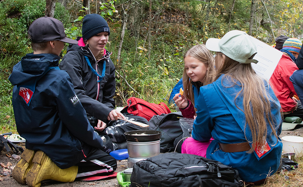 Kaksi poikaa ja kaksi tyttöä valmistamassa ruokaa retkikeittimellä metsäisellä polulla syksyllä.